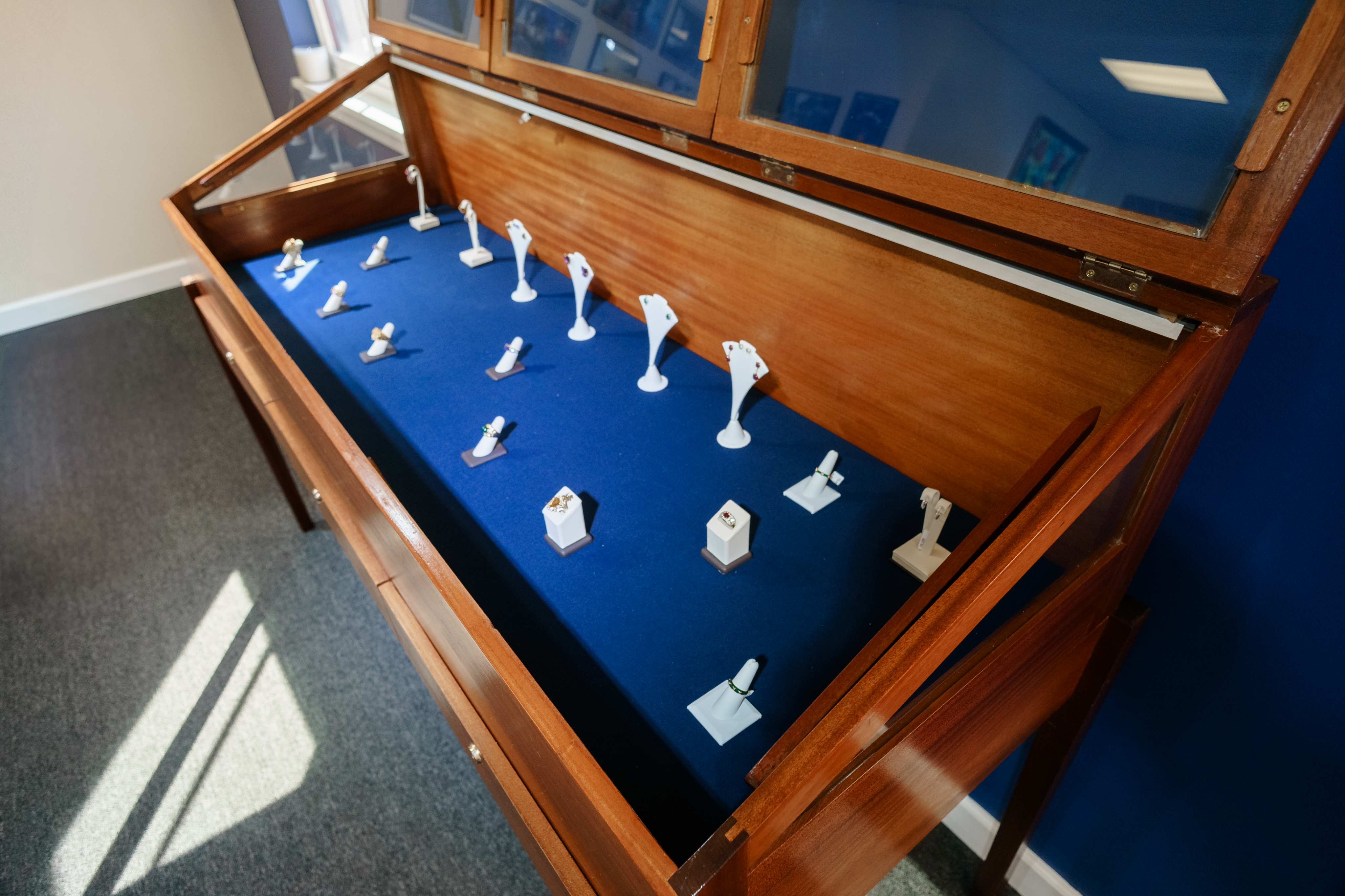 Coloured gemstone rings arranged on blue velvet inside a wooden display case