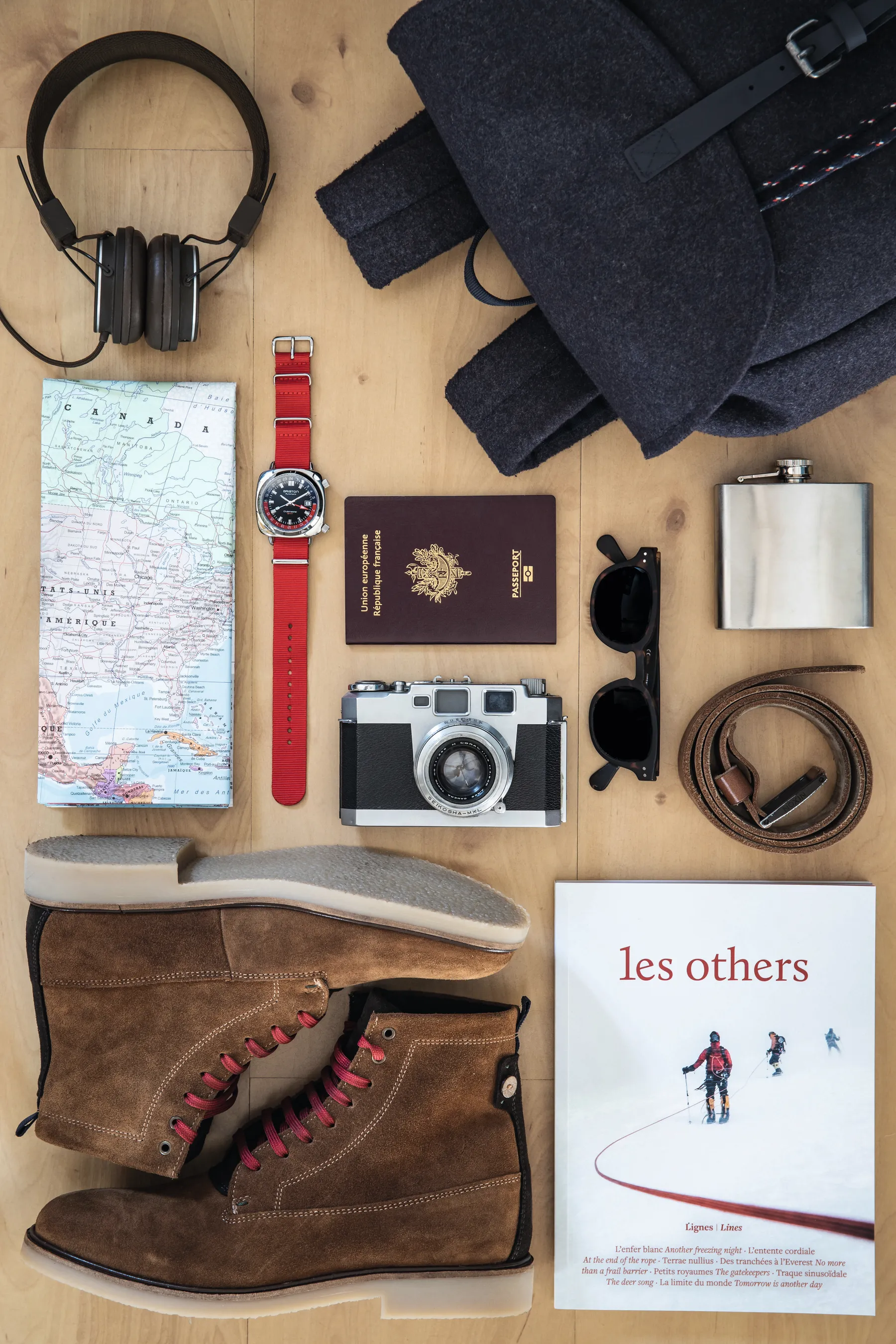 Briston GMT watch on a red NATO strap arranged with a passport, vintage camera and leather boots