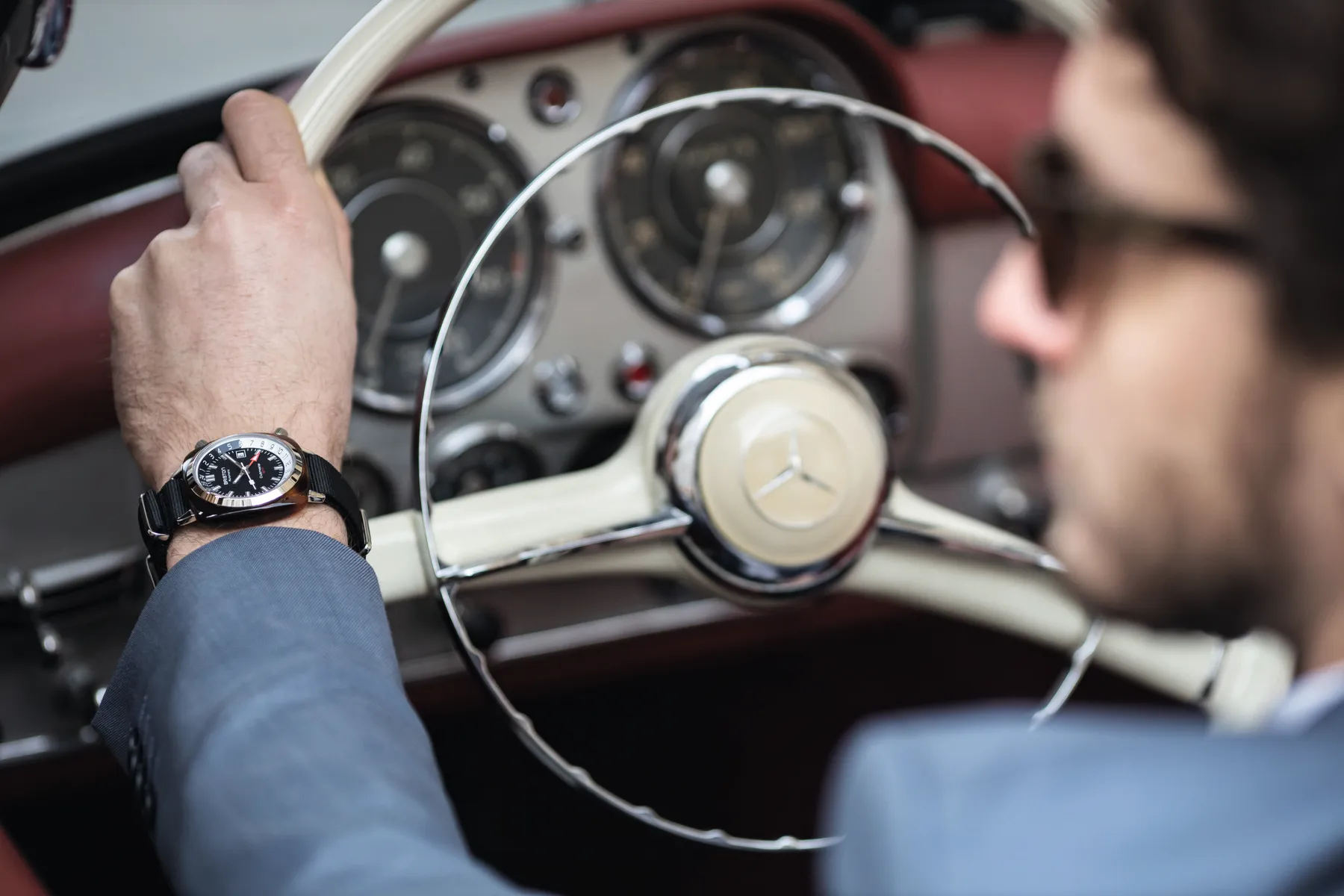 Flat lay of a Briston watch with leather boots, camera, passport and travel notebook