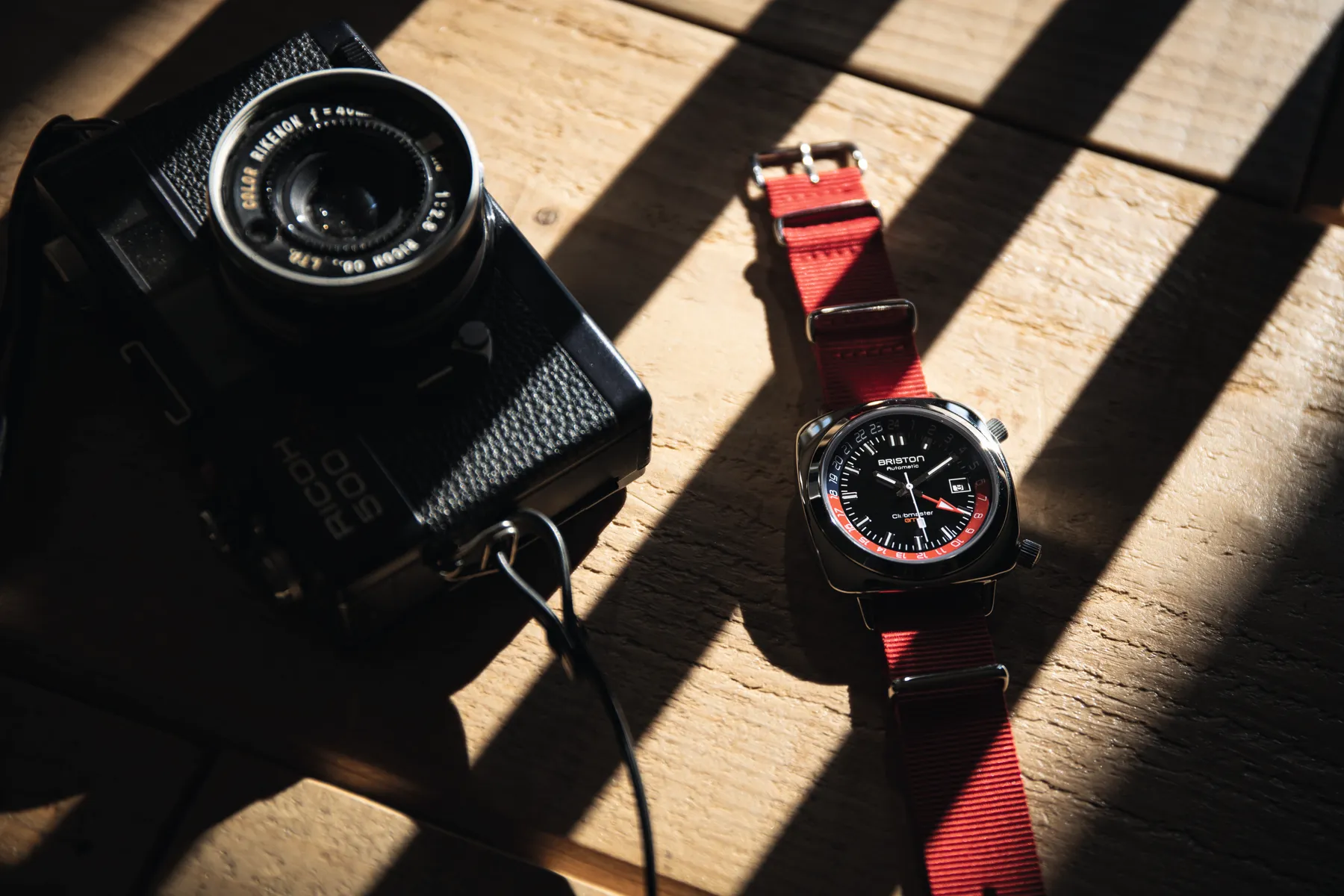 A wristwatch beside a vintage camera on a sunlit wooden table