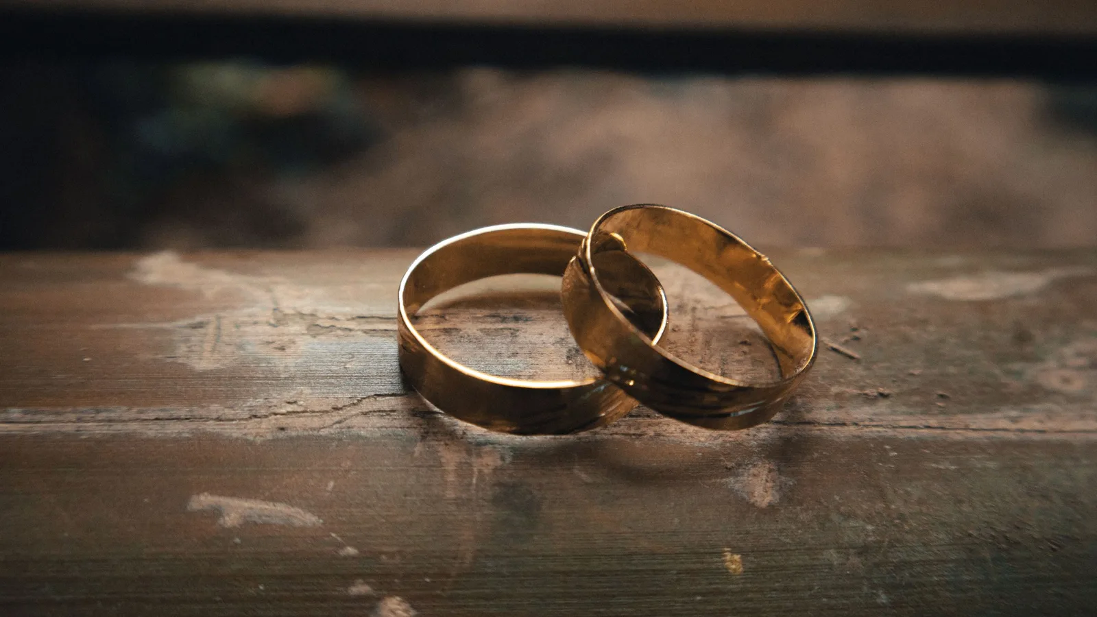 Two plain gold wedding bands resting together on a worn wooden surface