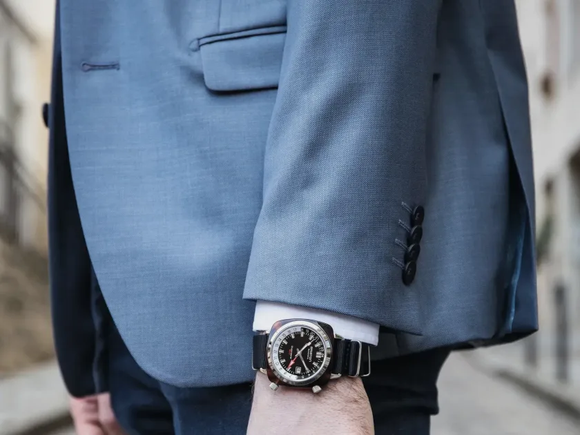 A wristwatch worn at the cuff of a blue suit jacket