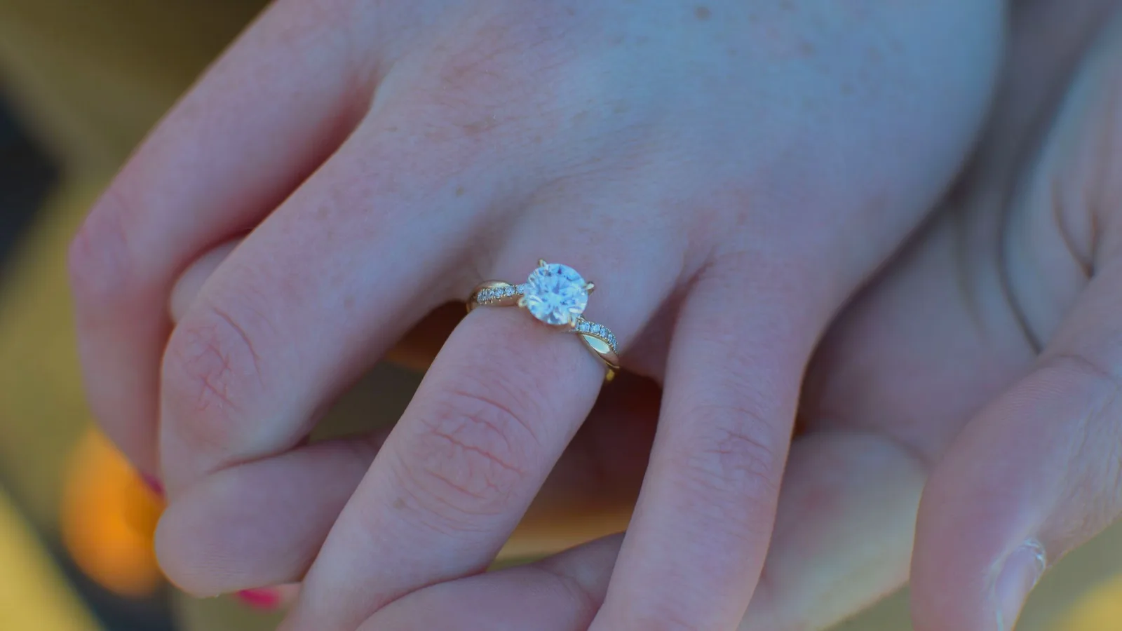 A diamond solitaire engagement ring held between two fingers