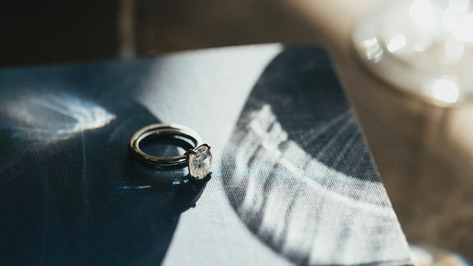 A solitaire diamond ring resting on the cover of an old book in warm raking light