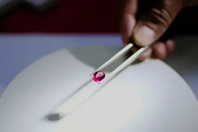 A loose gemstone held in tweezers under a lamp
