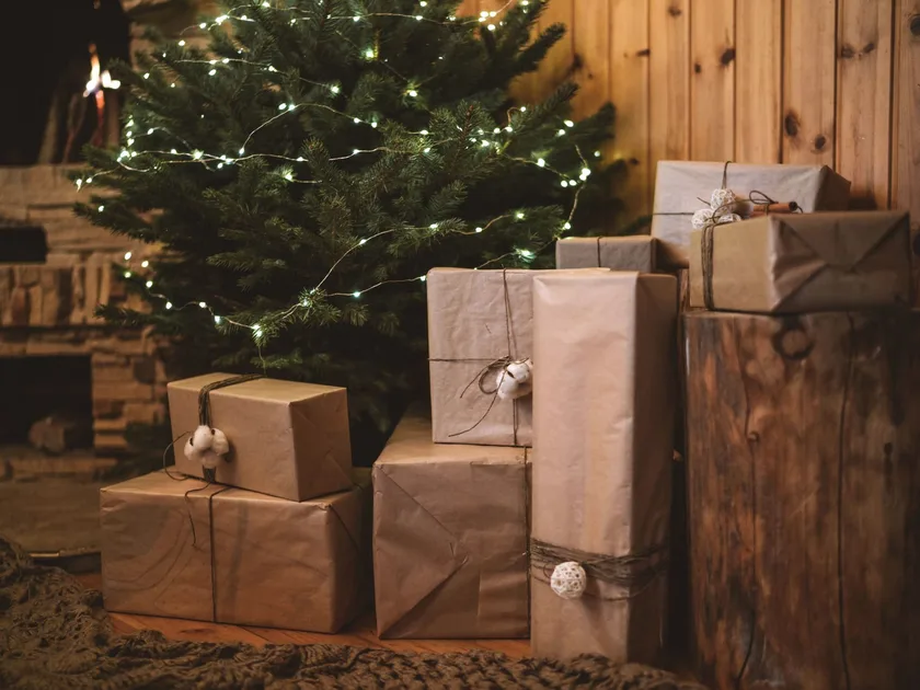 Wrapped gifts beneath a lit Christmas tree beside a fireplace