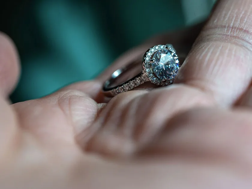 A halo diamond ring in a white metal setting held in the palm of a hand