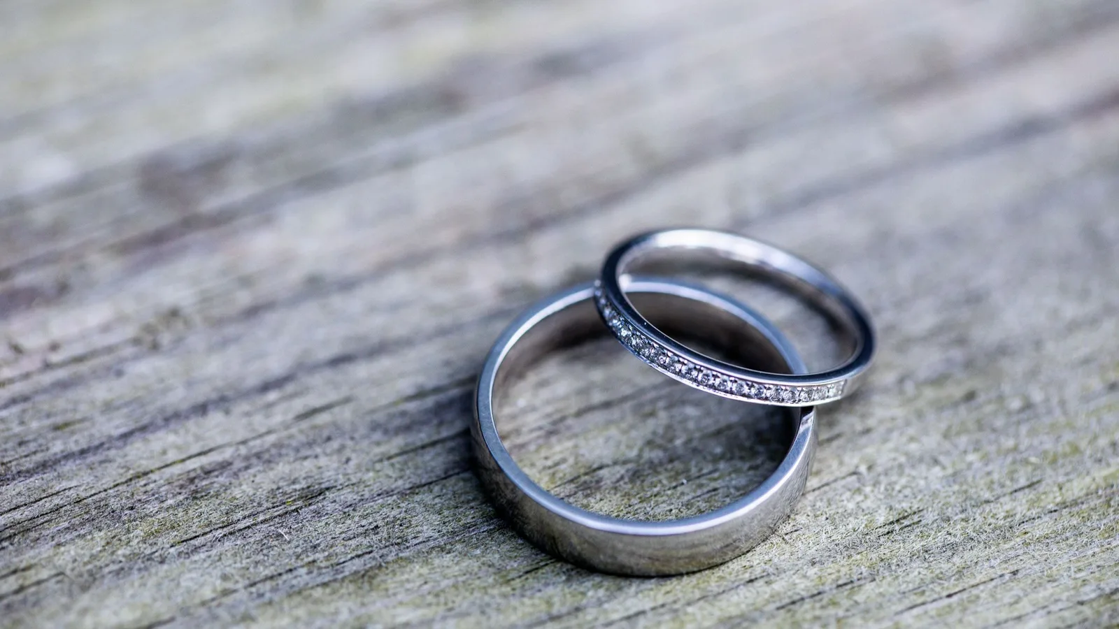 Two white metal wedding bands on weathered wood, a plain band and a thin band set with small diamonds