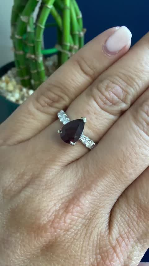 A pear cut ruby ring with diamond accents, worn on the hand