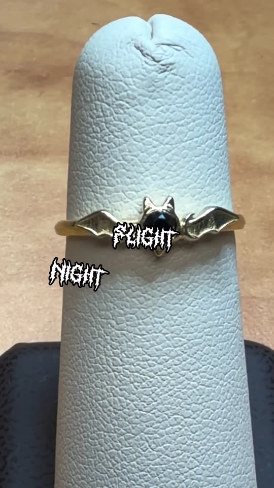 A gold bat ring set with a black diamond, worn on the hand
