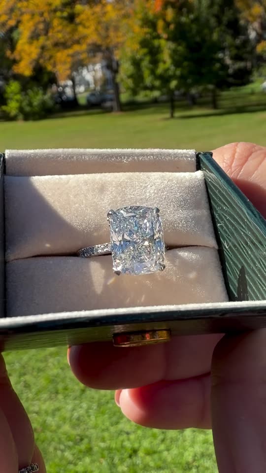 An elongated cushion diamond engagement ring lifted from its box in an autumn park