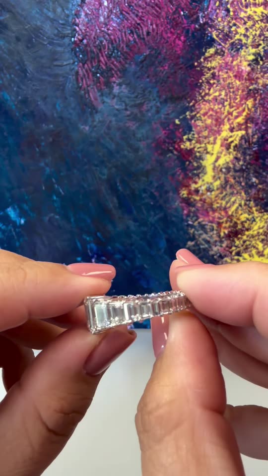 An emerald cut diamond ring with a band of step cut diamonds, worn on the hand