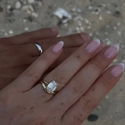 A yellow gold emerald cut solitaire and a plain band worn on two hands