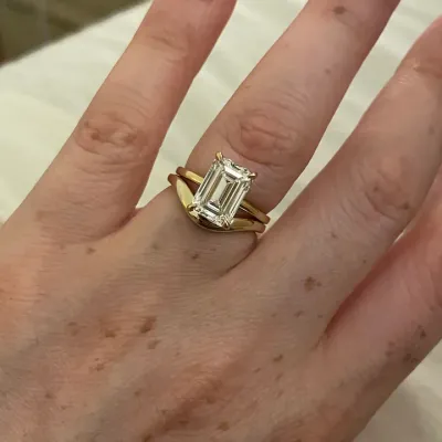 An emerald cut diamond solitaire in yellow gold with a fitted band beneath it