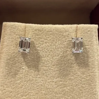 A pair of emerald cut diamond stud earrings on cream velvet