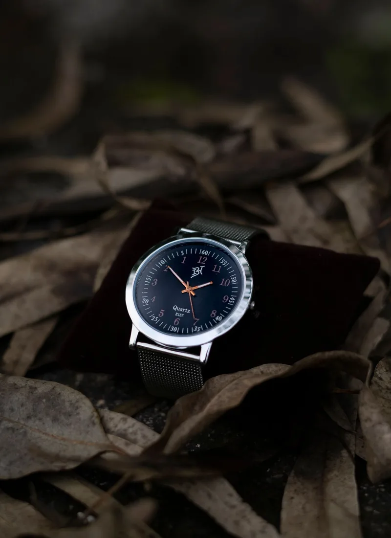A quartz wristwatch with a mesh bracelet resting on fallen leaves