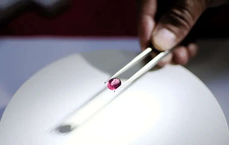 A loose gemstone held in tweezers under a lamp