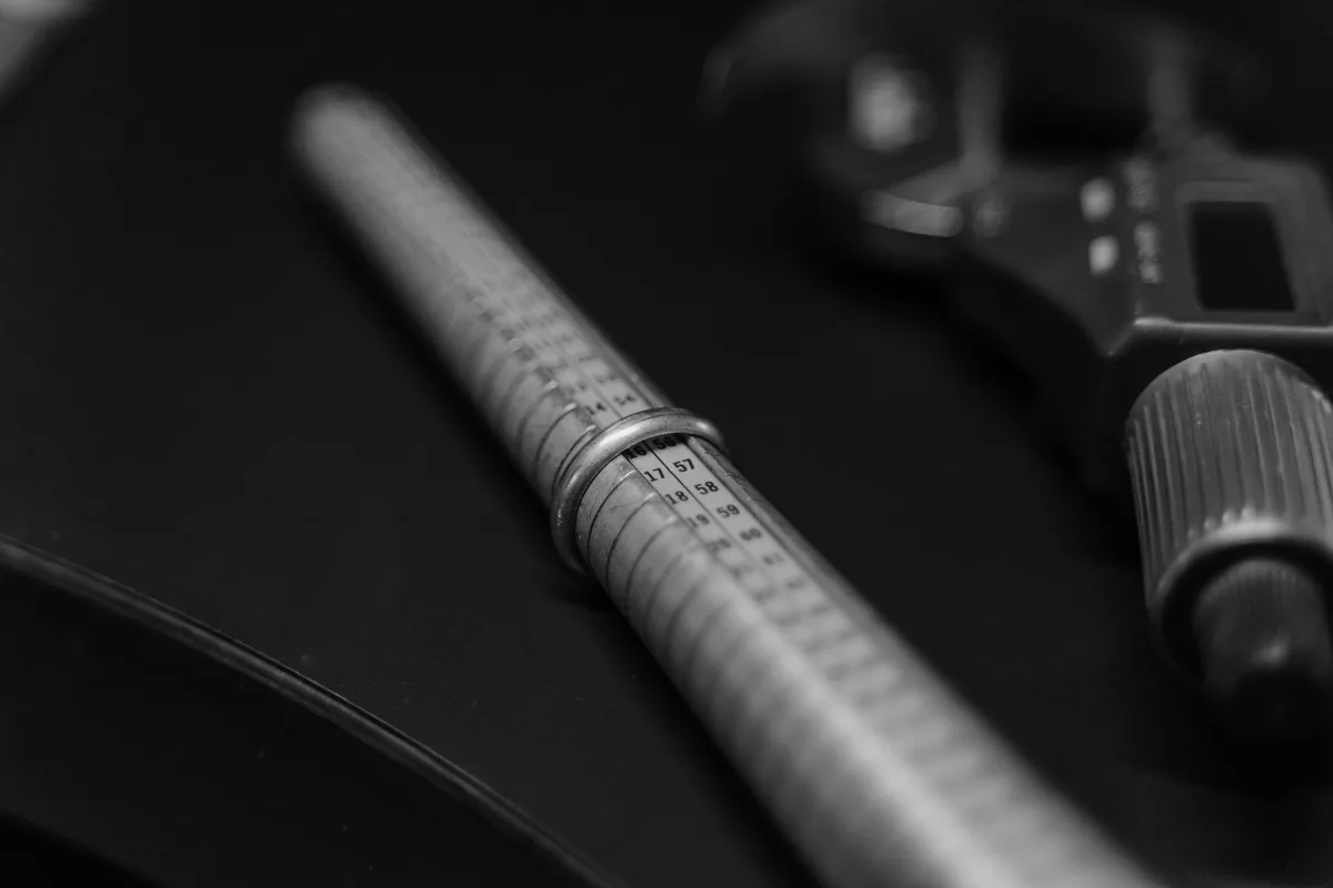 A ring sizing mandrel marked with sizes, resting on a dark surface