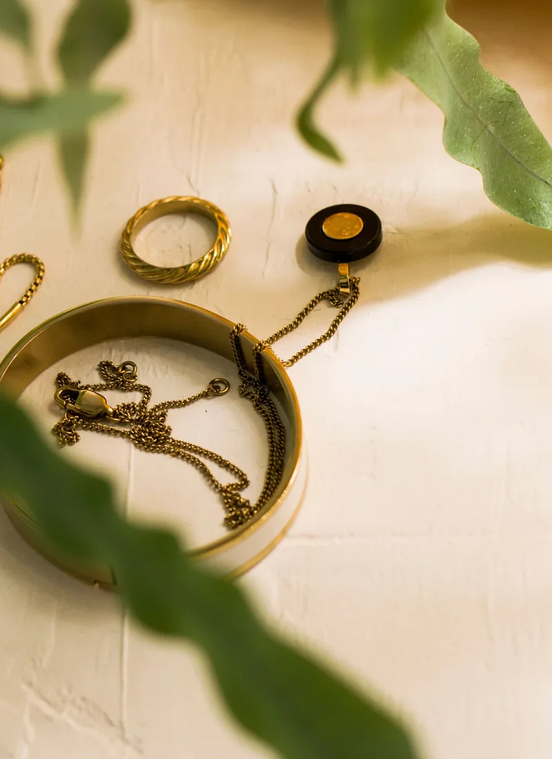 A gold bangle holding a tangled chain, beside a twisted ring and a small pendant