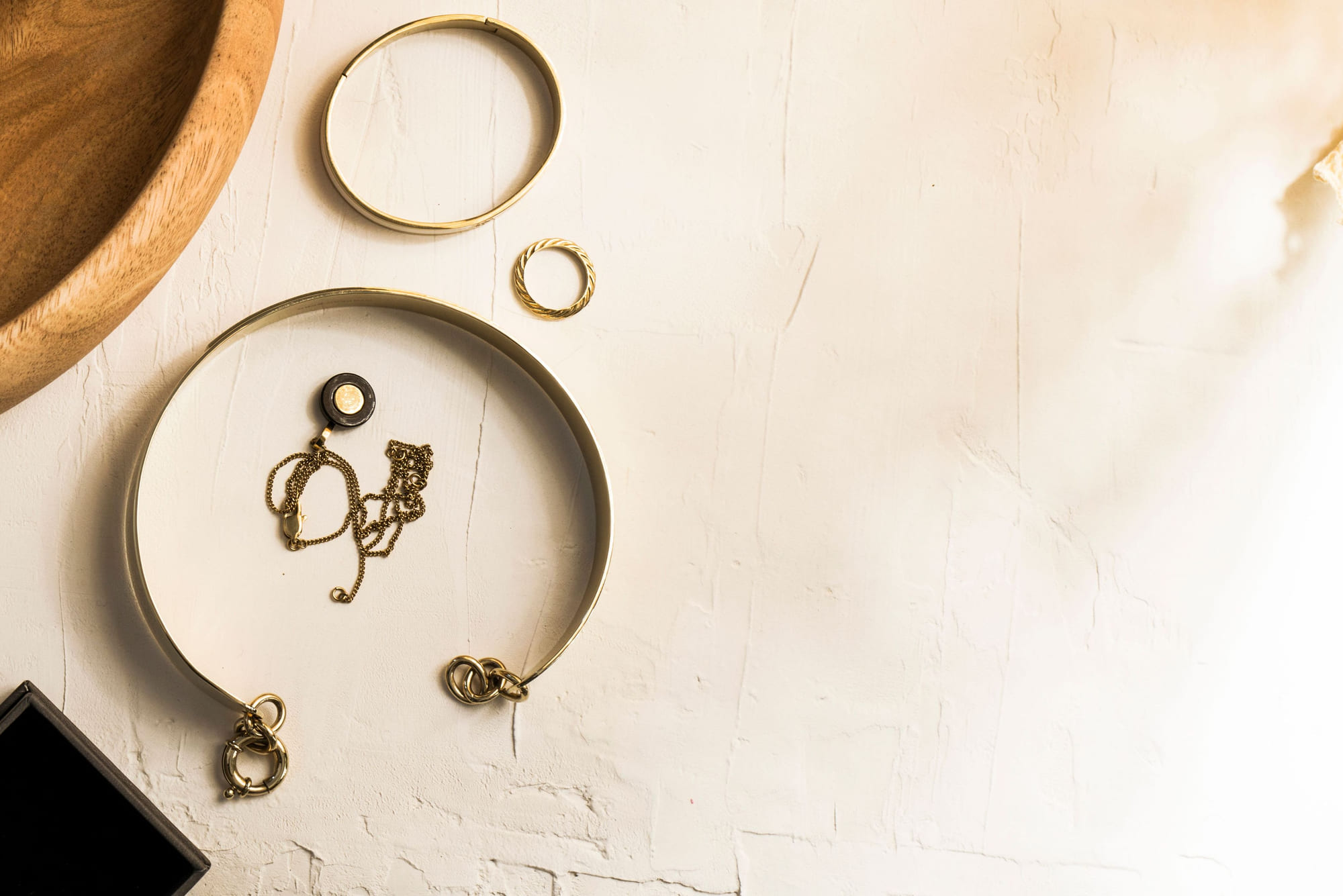 A gold bangle, a twisted gold ring and a fine gold chain laid out beside a wooden tray