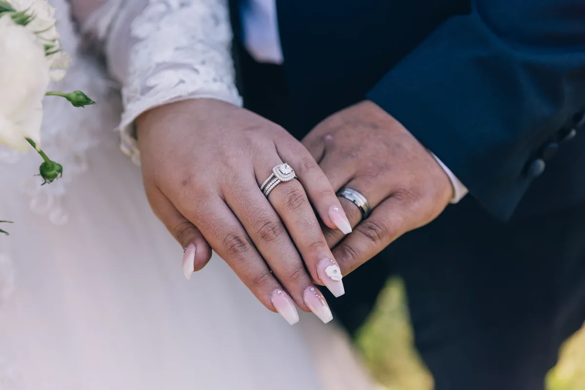 A halo engagement ring with a wedding band sitting flush beneath it, next to a wider band