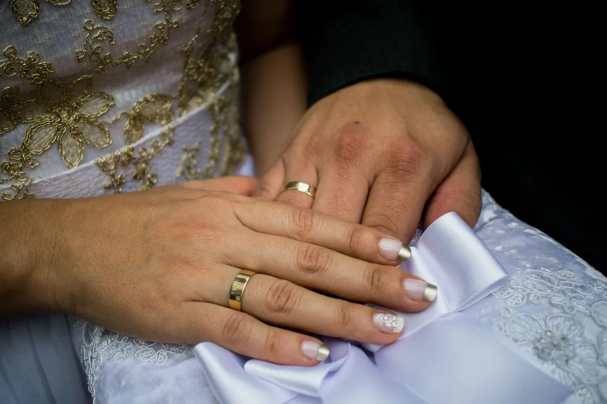 Two hands wearing plain gold wedding bands, one narrower than the other