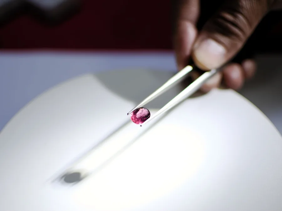 A loose gemstone held with tweezers under light