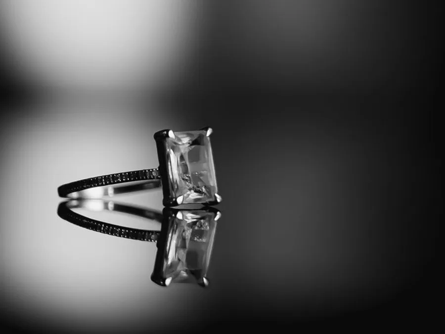 A diamond engagement ring reflected on a dark surface