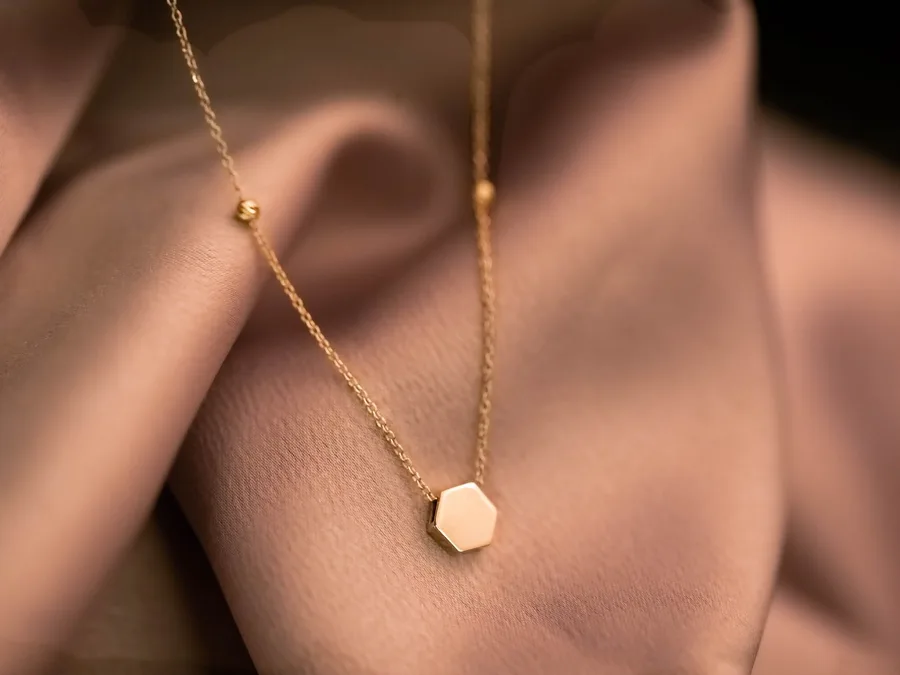 A gold necklace with a hexagon pendant on fabric
